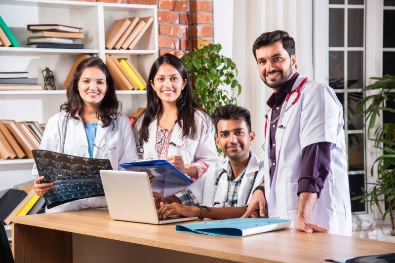 Successful Young Indian asian medical doctors are using a laptop and smiling while having a discussion at table